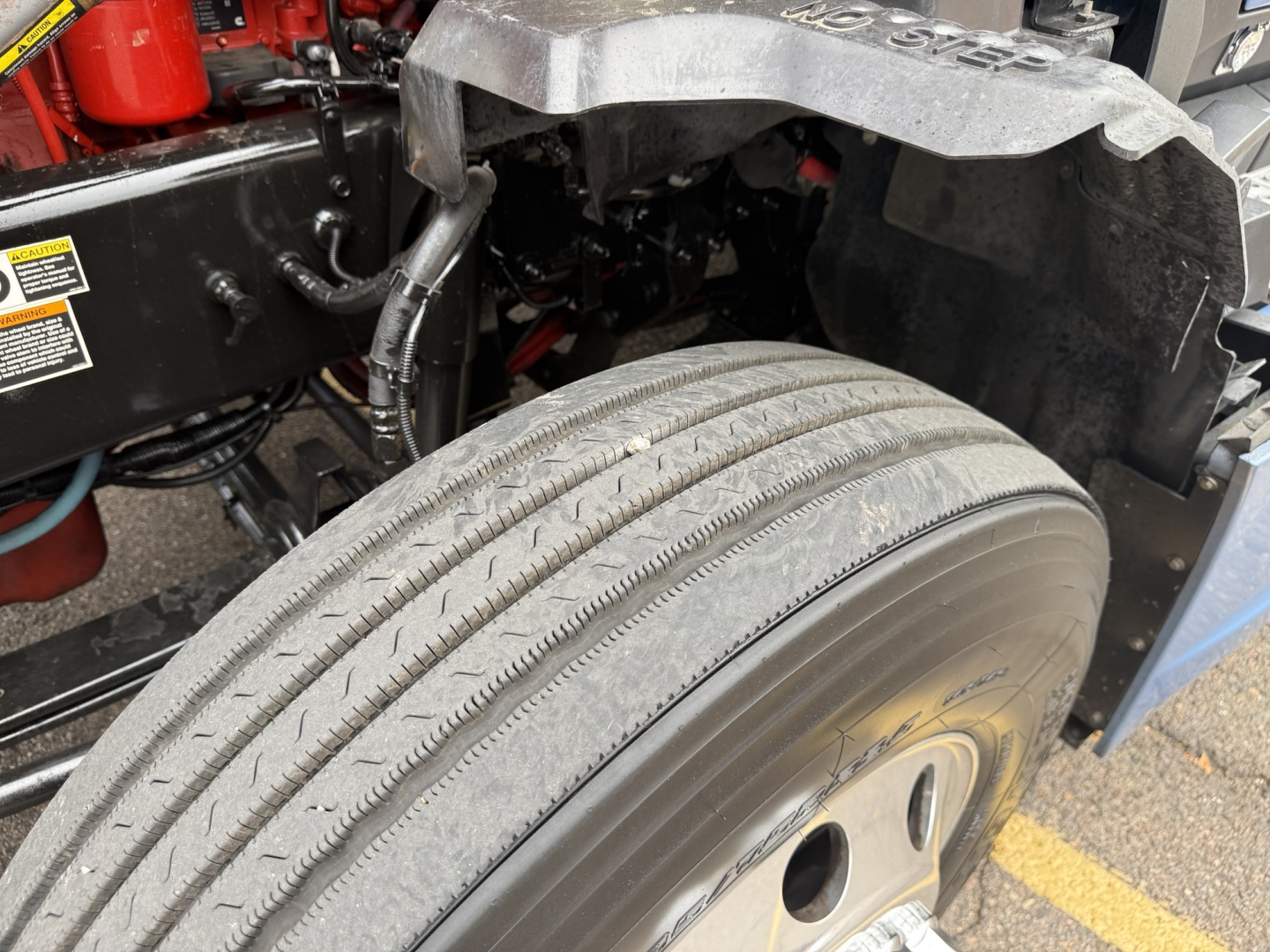 Kenworth T680 front wheel well and axle area with tire showing tread and wheel, partial chassis and components visible