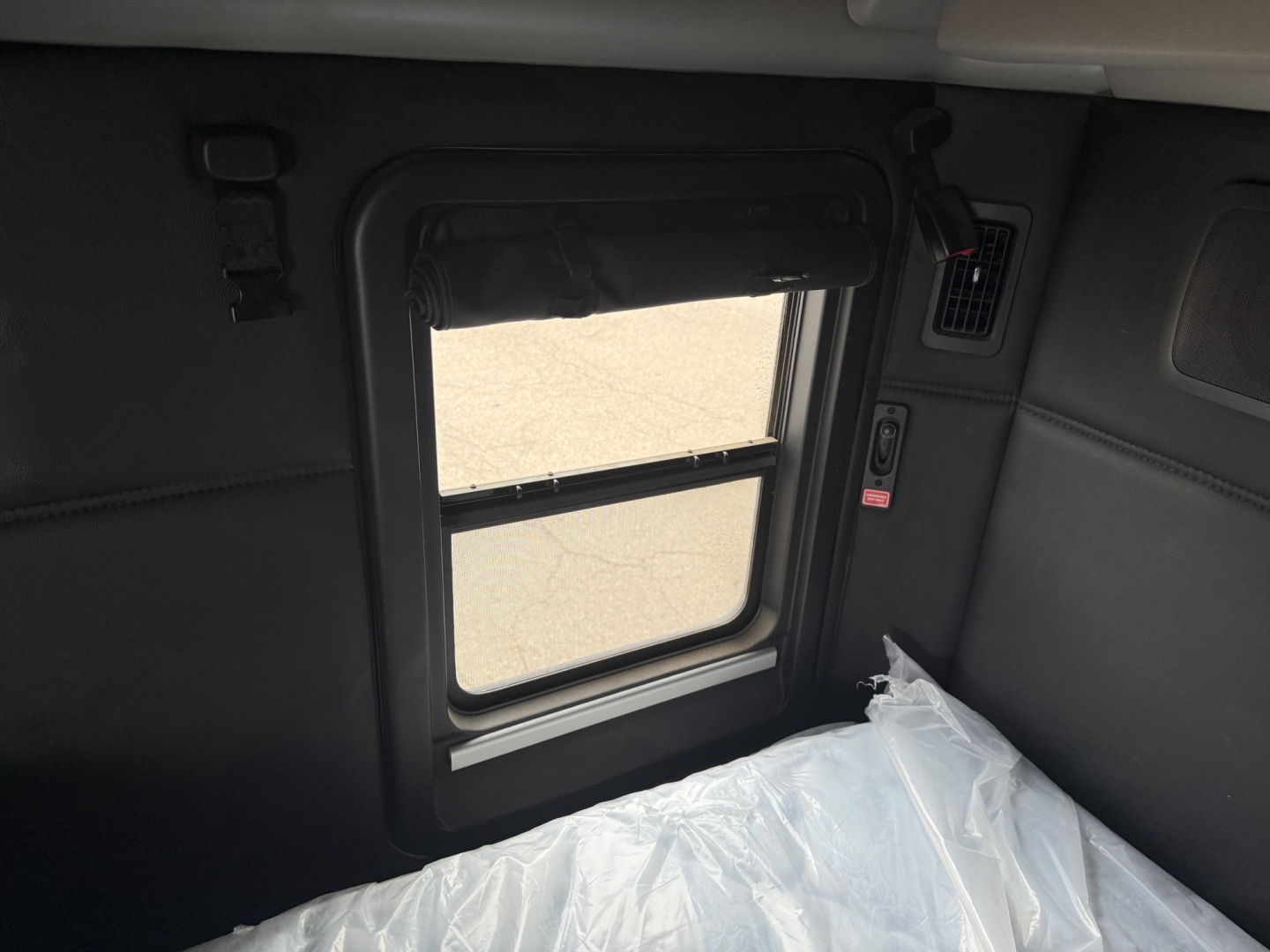 Kenworth T680 truck sleeper cab interior window with a sunshade and a plastic-covered seat area visible.