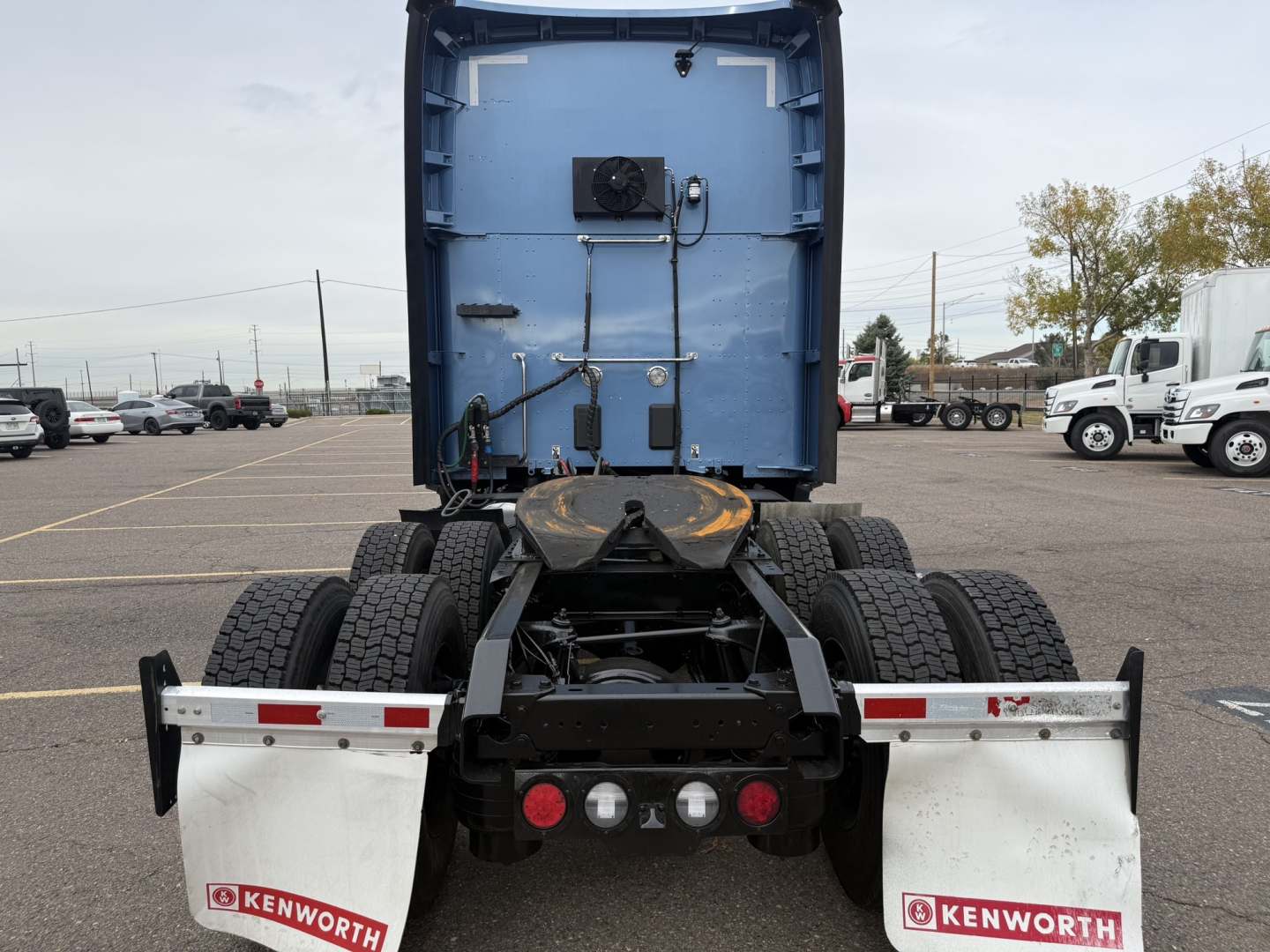 Kenworth T680 rear view showing fifth wheel, dual rear axles, and suspension; blue cab section with wiring and components mounted; Kenworth mud flaps and taillights visible.