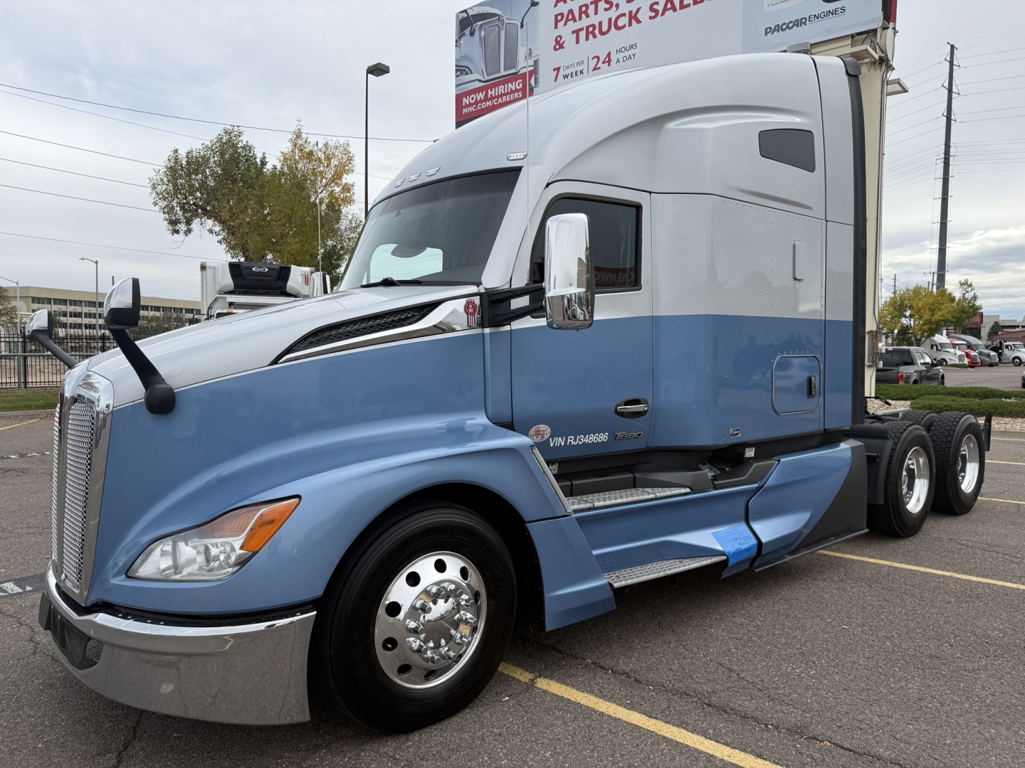 Kenworth T680 sleeper cab tractor in blue and gray with chrome wheels, side mirrors, and fuel tanks visible.