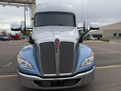 Kenworth T680 front view showing large dual grille with chrome surround, Kenworth emblem, blue fenders, silver bumper, side mirrors, and windshield. No visible text other than truck design.