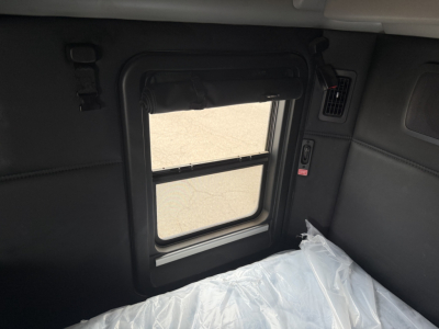 Kenworth T680 truck sleeper cab interior window with a sunshade and a plastic-covered seat area visible.