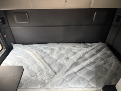 Kenworth T680 sleeper cab interior showing bed with plastic-covered mattress, side cabinets, and window blinds.