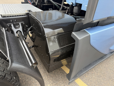 Kenworth T680 side view showing engine bay area with metallic toolbox and exposed chassis components.