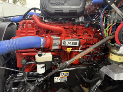 Kenworth T680 engine bay showing X15 Cummins engine and PACCAR branding with blue intercooler hose and various colored wiring.