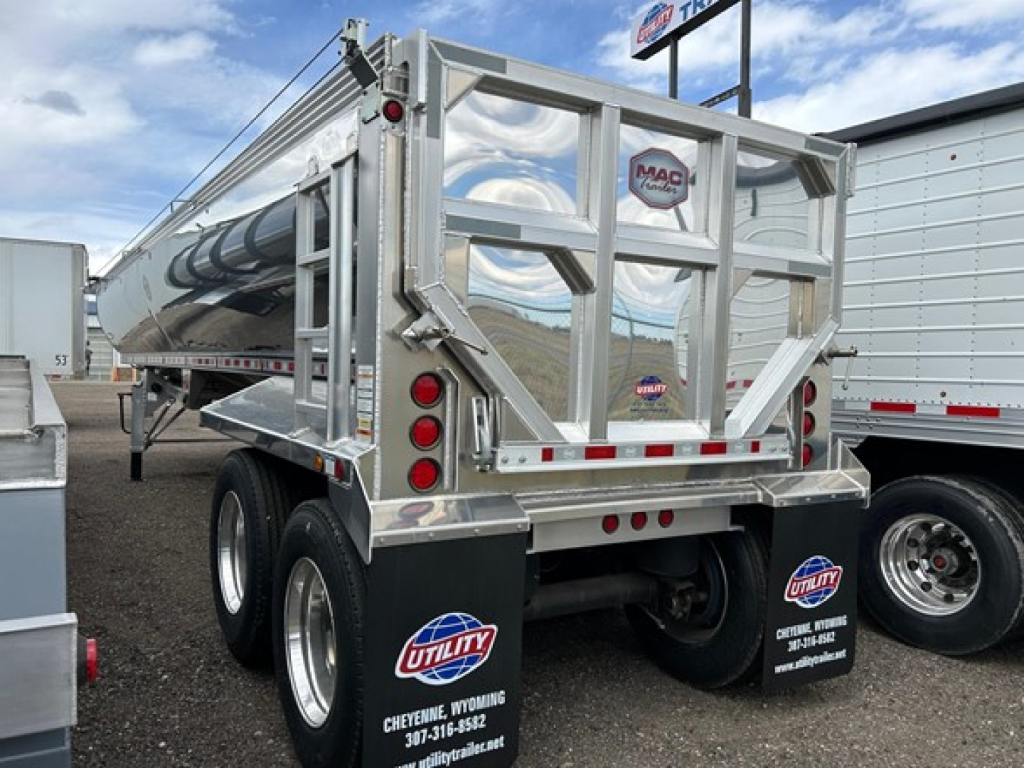 Dump trailer rear view showing tandem axles, reflective tape, MAC trailer logo, and chrome metal framework with rear access gate.
