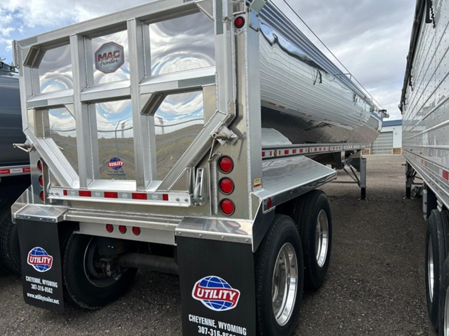 Dump trailer rear view showing MacMacsimiser logo on back gate, chrome-alloy frame, dual rear wheels, and utility plate; polished metal surface with reflective tape.