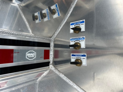 Control panel inside a Mac Trailers dump trailer showing knobs labeled Lift Style, Suspension Dump, Tailgate with blue labels and black handles; Mac logo on red and silver strip.