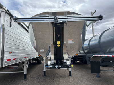 Frameless aluminum end dump trailer, front view, with hydraulic landing gear and top guide arms, reflective tape, and surrounding trailers.