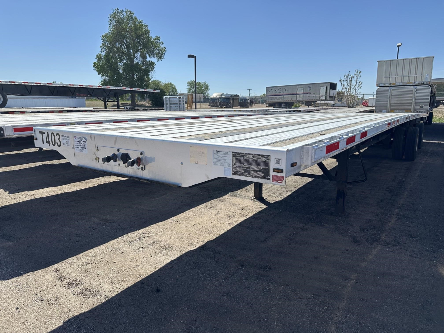 Transcraft combo flatbed trailer in-view showing long aluminum deck with reflective safety tape and rear wheels; front left shows license plate-like plate with numbers.