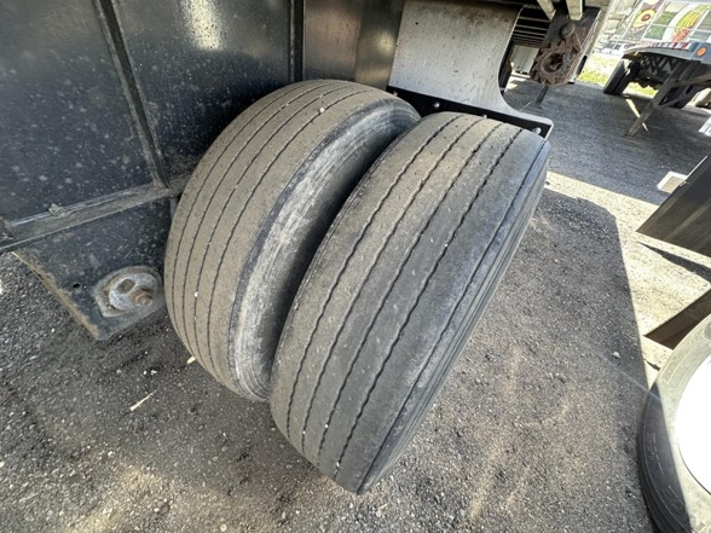Dual rear trailer tires mounted on Transcraft flatbed trailer axle, visible undercarriage and frame.