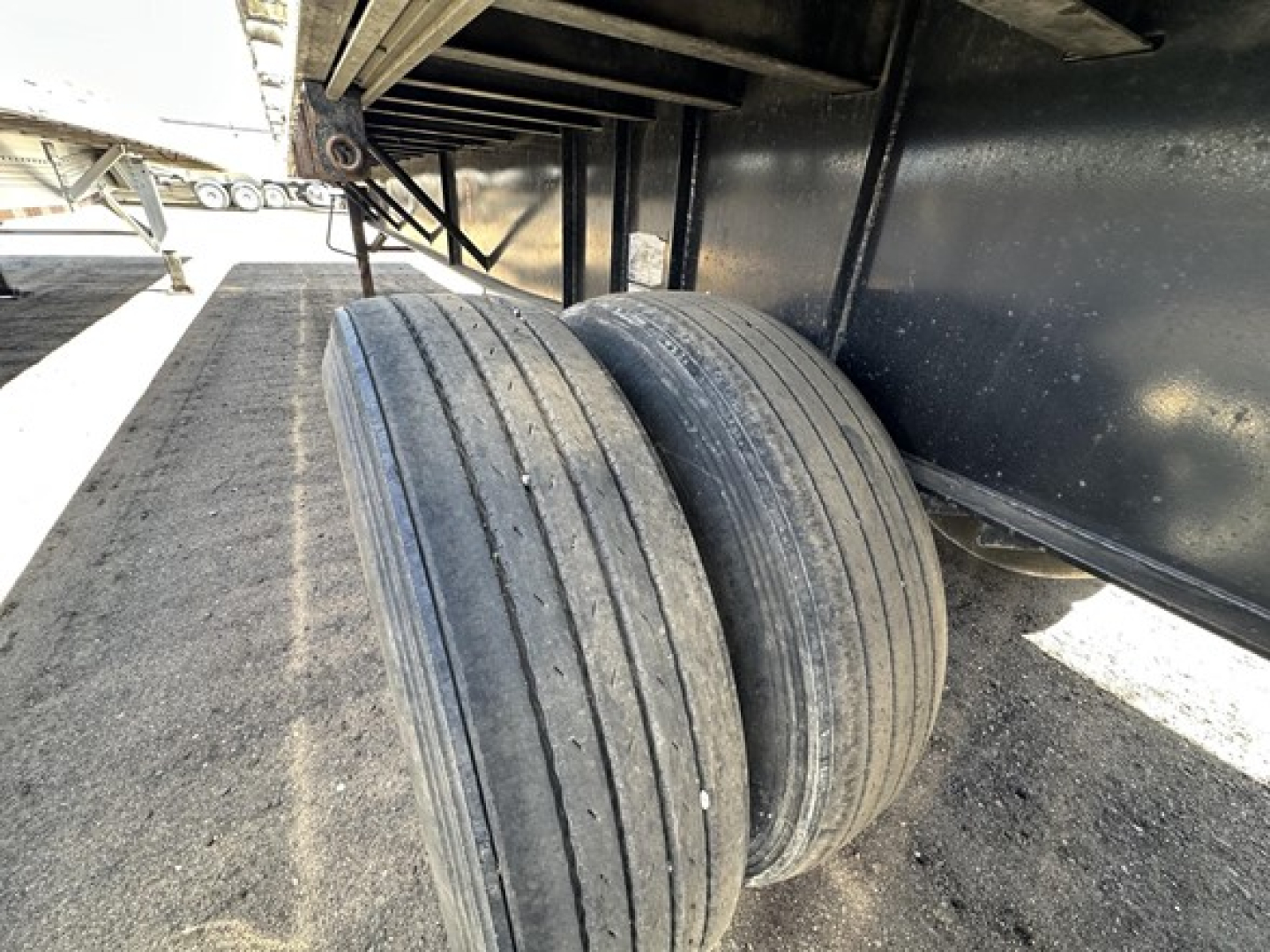 Trailer wheel assembly showing dual rear axles and tires on a flatbed trailer frame.