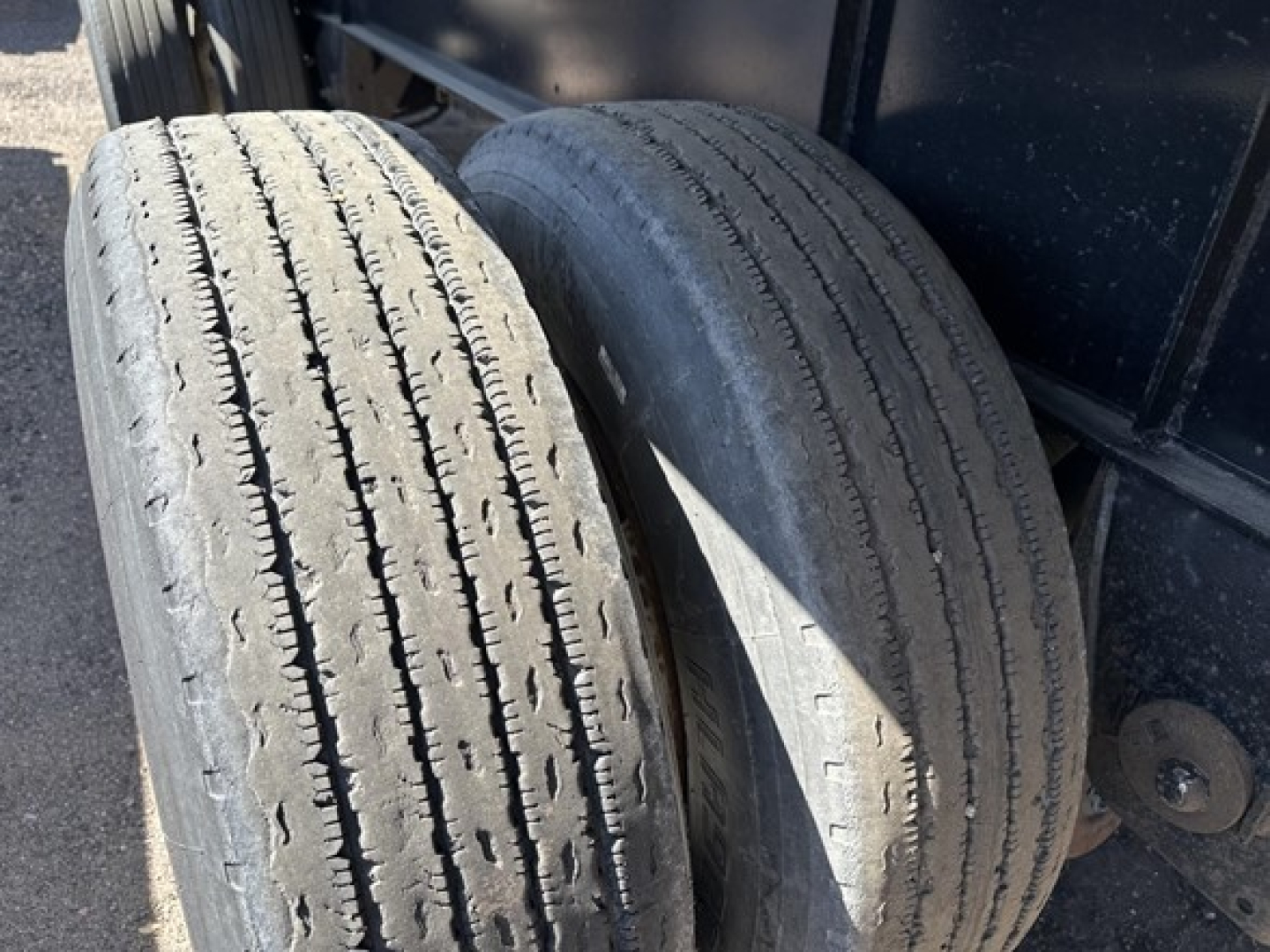 Two used trailer tires mounted on a Transcraft flatbed trailer undercarriage showing tread wear and sidewall details.