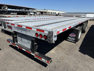 Flatbed trailer rear and side with metal deck, red and white reflective tape, multiple taillights, spare tire, and mudflaps showing ‘Utility Trailer’ mudflap branding.