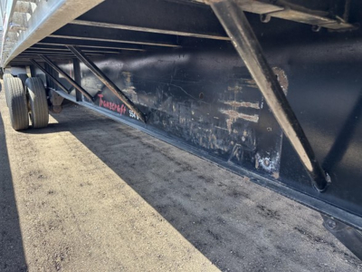 Flatbed trailer undercarriage with Transcraft branding on the side near the wheel. Text visible includes 'Transcraft' in pink on the black side of the trailer.