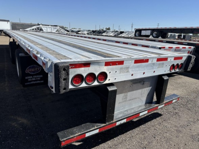 Flatbed trailer with extendable air combo system showing rear end, taillights, and reflective tape; metal deck; utility stickers visible.