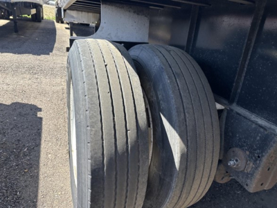 Trailer axle area showing dual rear tires on Transcraft flatbed trailer, undercarriage and frame visible.