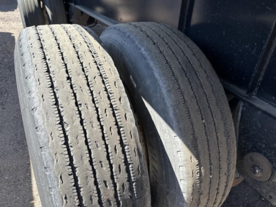 Two used trailer tires mounted on a Transcraft flatbed trailer undercarriage showing tread wear and sidewall details.