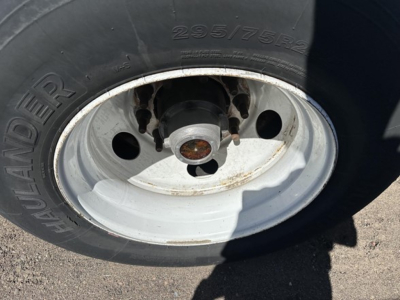 Trailer wheel and tire with 295/75R22.5 tire, white steel rim, wheel hub with rust on studs.