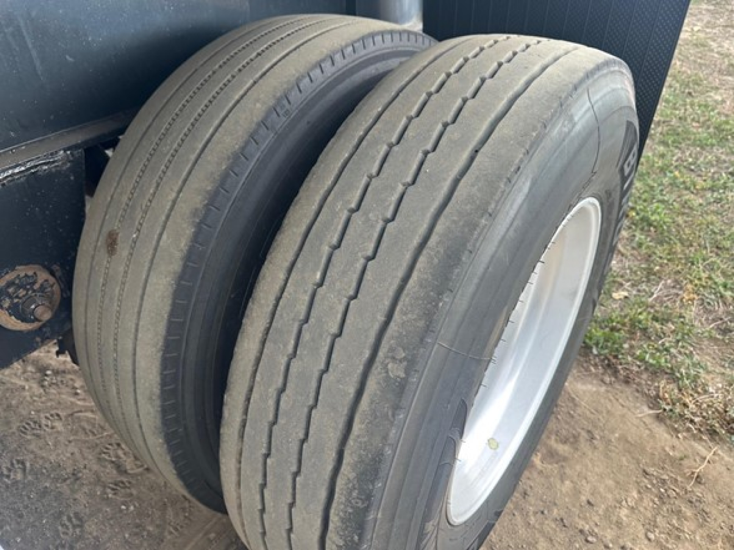 Trailer axle with dual tires showing wear and sidewall inscriptions