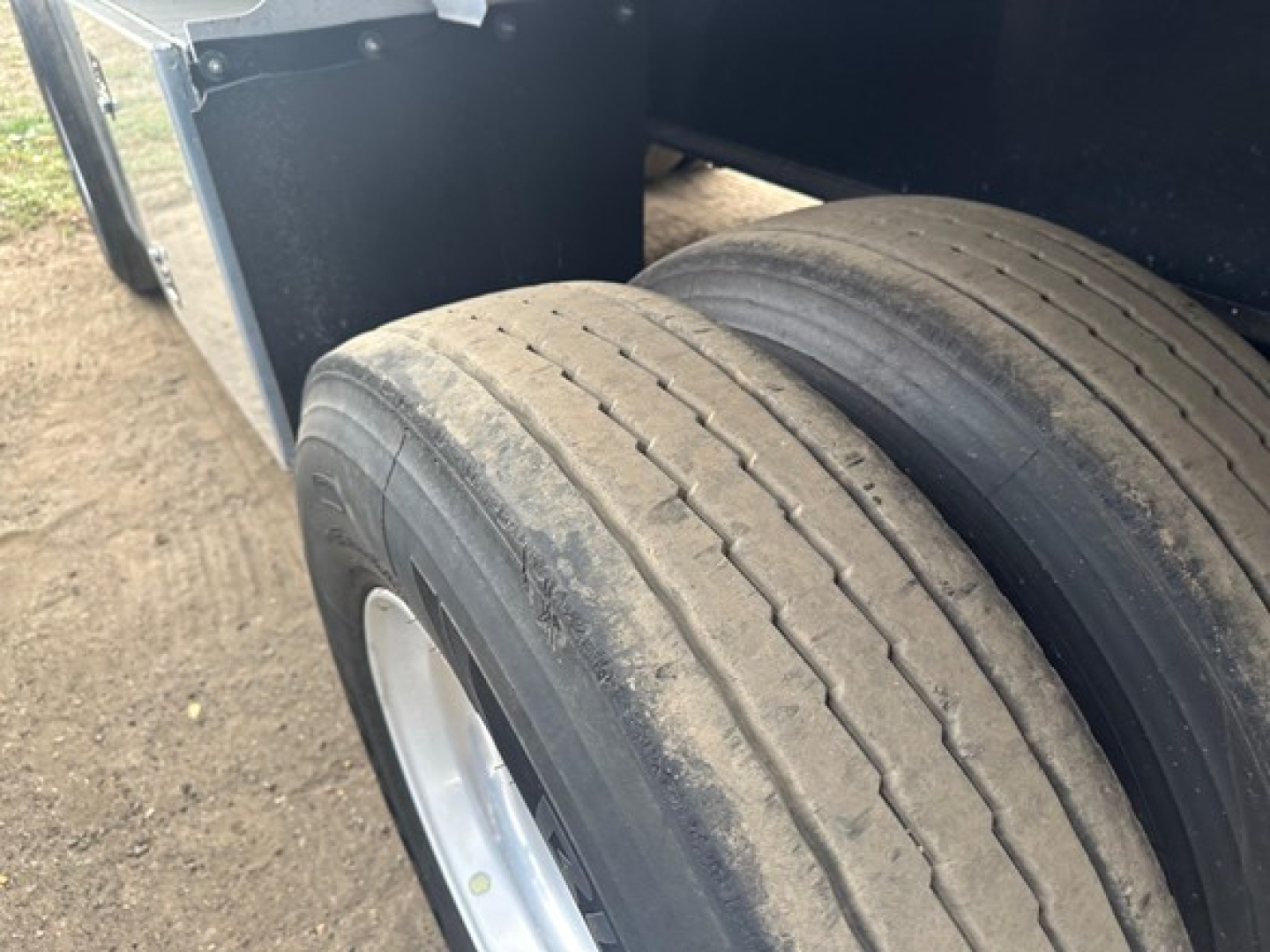 Trailer axle and dual tires on a flatbed cargo trailer showing treaded tires and part of wheel well.