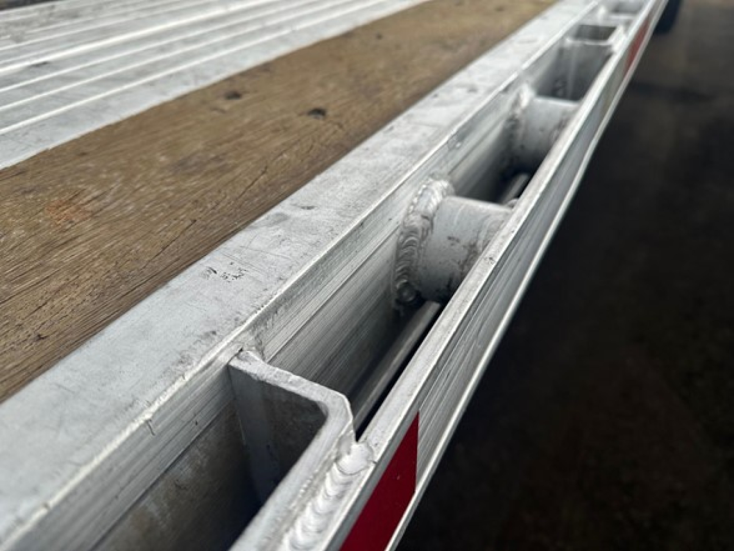 Trailer bed edge with aluminum side rail and wood deck showing stake pocket and t-slot channel.