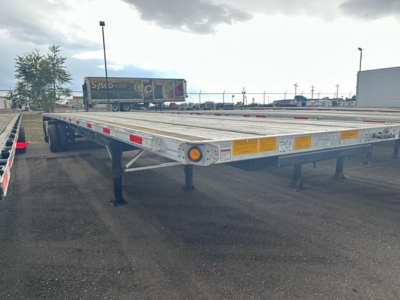 Flatbed trailer showing low deck and side marker lights, reflective tape, and support legs visible.