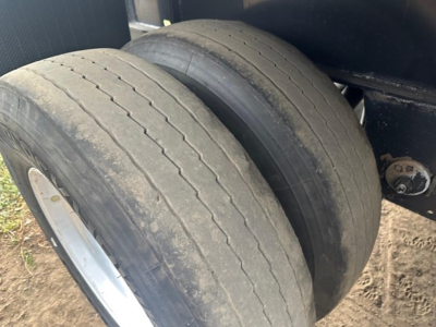 Trailer wheel pair with dual tires mounted on axle under flatbed trailer. Visible tread wear marks on one tire.