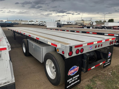 Trailer rear and side view of a Utility 4000Ae flatbed trailer showing dual rear wheels, metal deck, taillights, and utility branding.