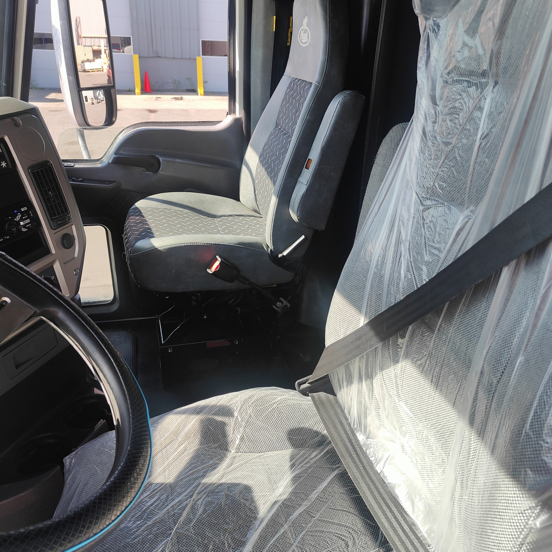 Truck cab interior of a 2016 Mack CXU613 showcasing driver seat, passenger seat, and seat belts.