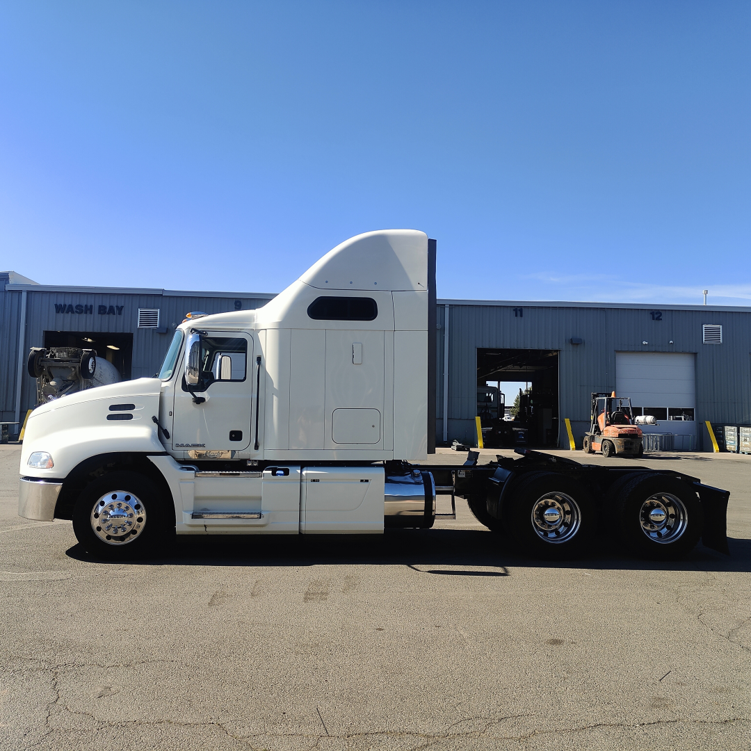 Truck side view showing a white 2016 Mack CXU613 sleeper cab tractor with dual rear axles and chrome wheels.