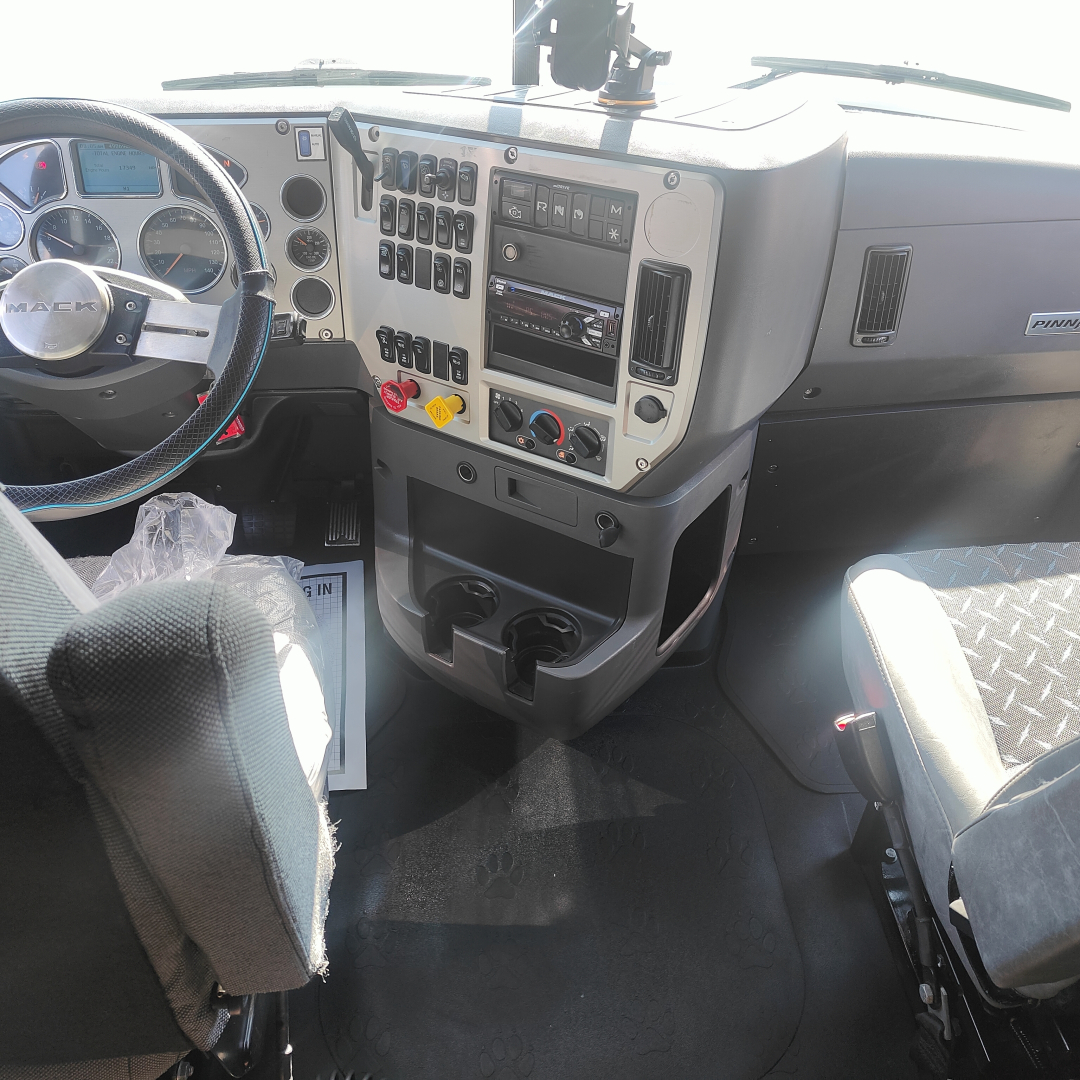 Truck cab interior showing steering wheel, instrument cluster, and center console with numerous controls. Dashboard has various labeled switches and a built-in radio. Cup holders and footwell visible.
