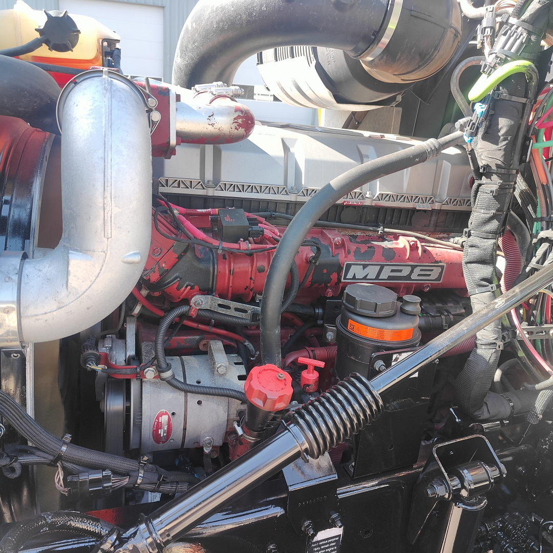Mack CXU613 engine bay showing MBP turbo piping and red engine block with visible belts and hoses.