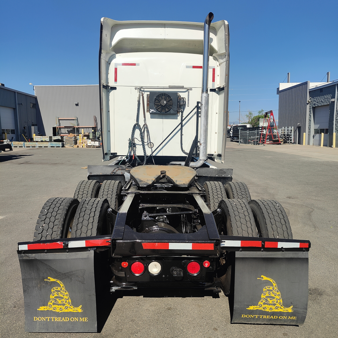 Rear view of a white Mack CXU613 sleeper tractor showing dual rear axles and fifth-wheel area. Mudflaps with “DON'T TREAD ON ME” and various lights.