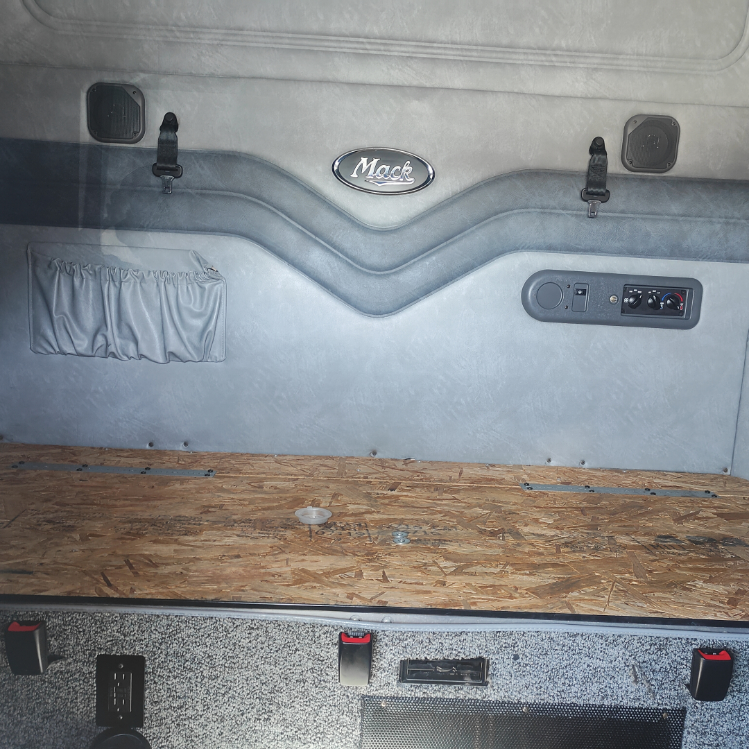 Mack CXU613 sleeper cab interior showing rear wall with Mack emblem, storage pocket, and controls with a wooden sleeper floor.