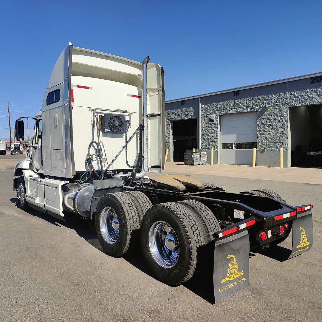 2016 Mack CXU613 sleeper tractor shown from rear-left side, focus on chassis and dual rear axles with mud flaps; cab interior visible through open door, no trailer attached.