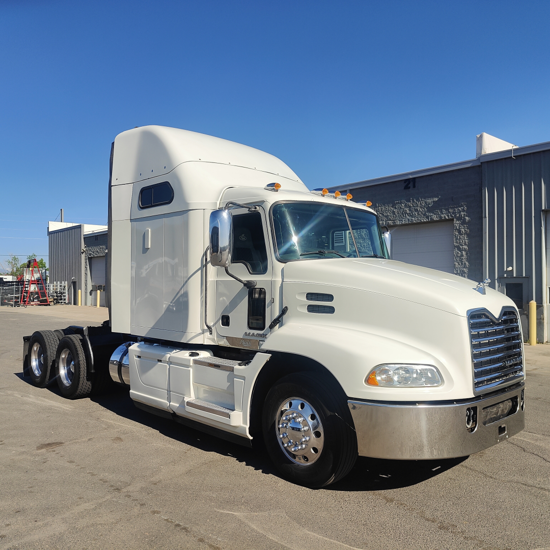 White 2016 Mack CXU613 conventional sleeper truck viewed from side-front angle show chrome bumper, twin rear axles, and sleeper cab