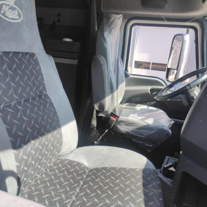 Truck cab interior of a 2016 Mack CXU613 showing driver seat and steering wheel with plastic seat covers, visible side window, doorway, and dashboard features.