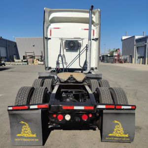 Rear view of a white Mack CXU613 sleeper tractor showing dual rear axles and fifth-wheel area. Mudflaps with “DON'T TREAD ON ME” and various lights.
