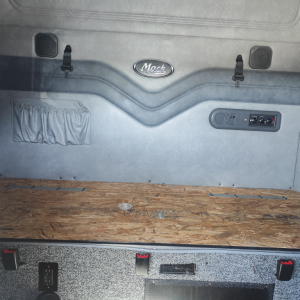 Mack CXU613 sleeper cab interior showing rear wall with Mack emblem, storage pocket, and controls with a wooden sleeper floor.