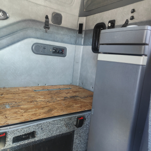 Truck cab interior of a 2016 Mack CXU613 sleeper showing side wall with storage, controls, and a raised plywood floor in the cargo area.