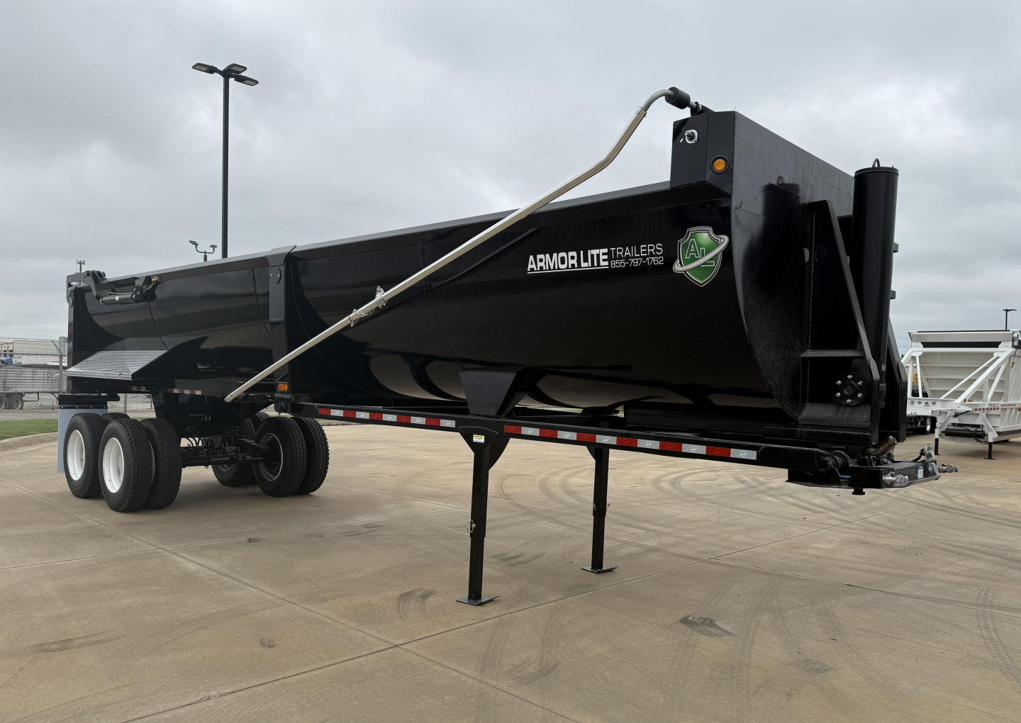 Armor Lite SHD32/48 dump trailer showing side view with black steel body, tandem axles, support leg, and hitch; decals read ARMOR LITE TRAILERS.