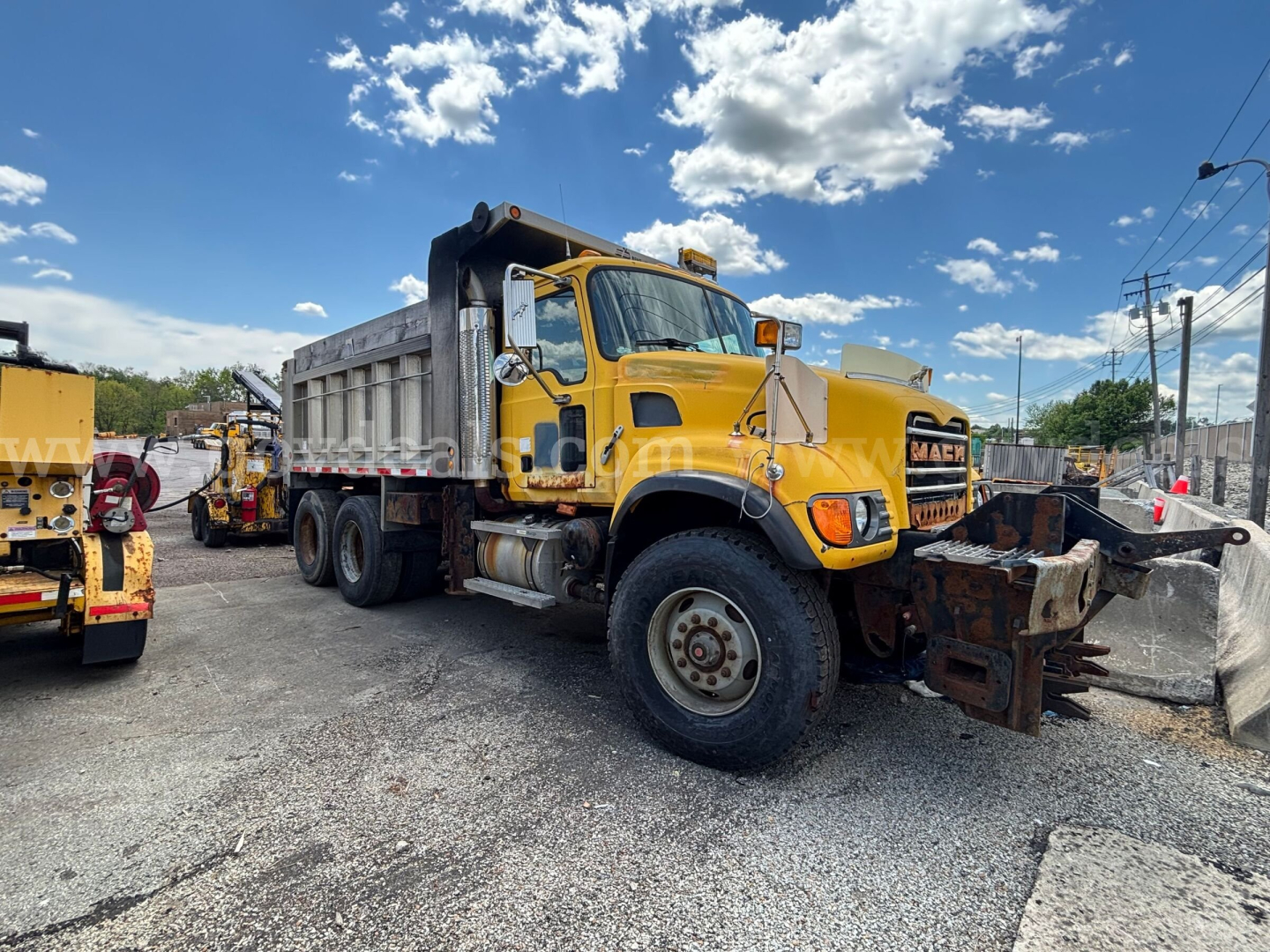 Dump truck 2006 Mack CV713 in service showing dump bed and front snowplow attachment with yellow cab and heavy-duty tires.