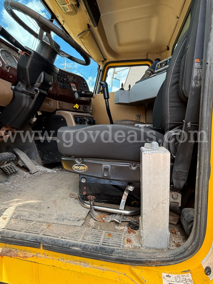Cab interior of a 2006 Mack CV713 dump truck showing steering wheel, dashboard, and driver seat with a Sealy seat base; floor and side steps visible.