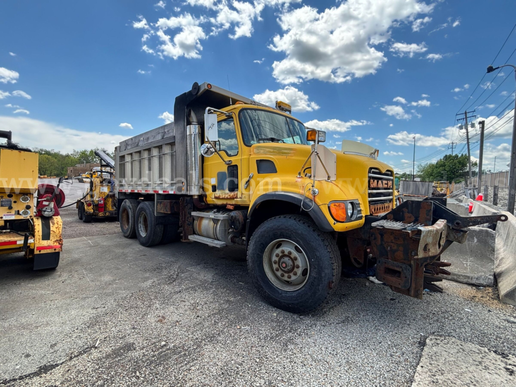 Dump truck 2006 Mack CV713 in service showing dump bed and front snowplow attachment with yellow cab and heavy-duty tires.