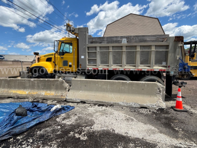 Yellow Mack CV713 dump truck in service with dump bed, side panels, and front cab visible; construction barriers and traffic cone in foreground.