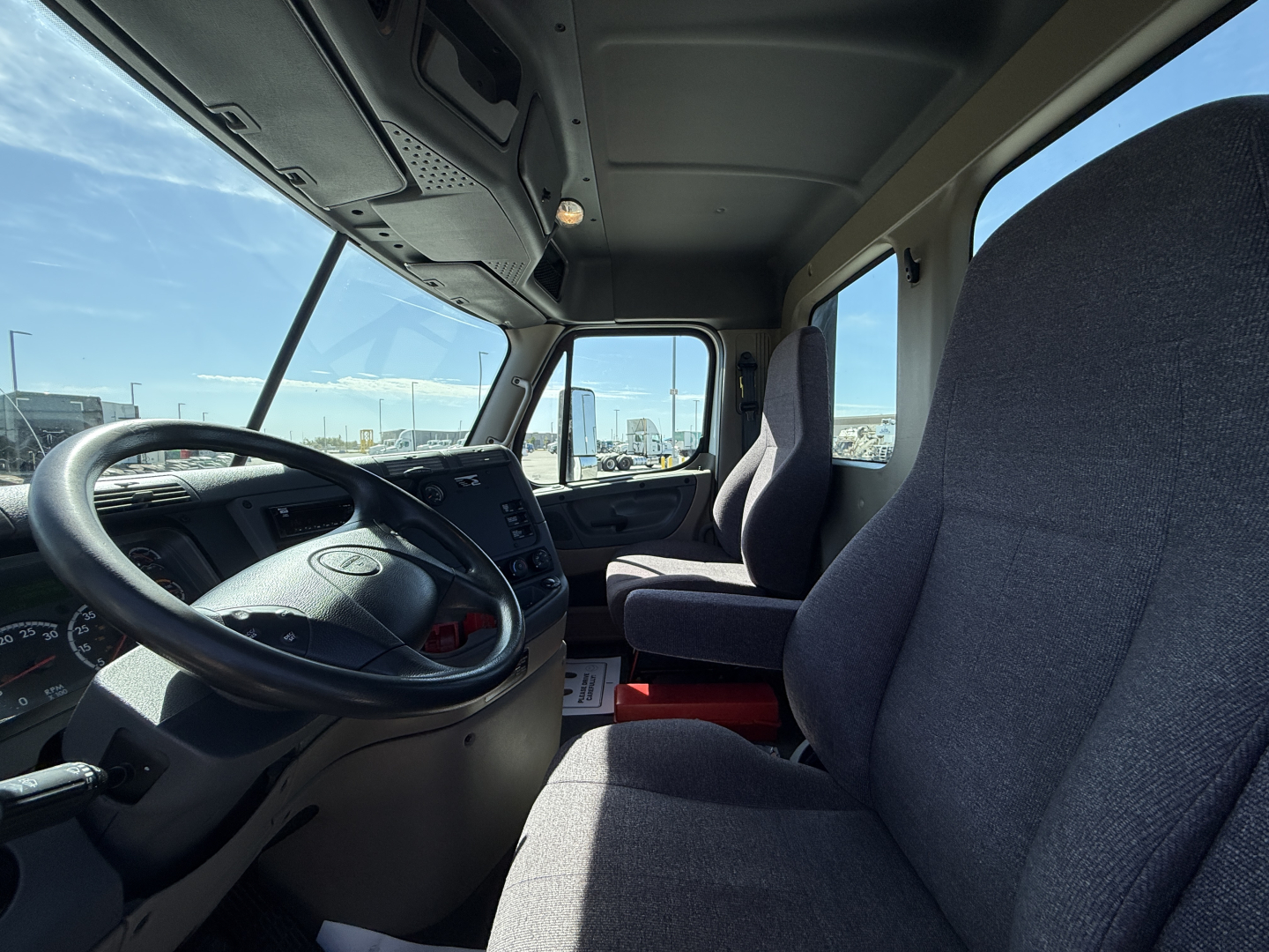Truck cab interior showing steering wheel, driver seat, and dashboard in Freightliner CA11364DC with windshield and side window view.