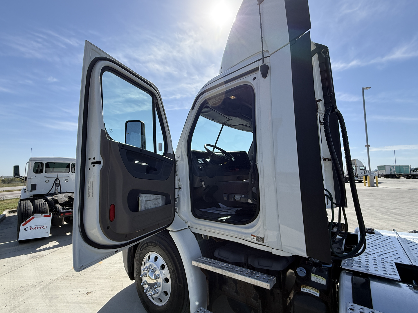 Truck cab door open showing Freightliner CA11364DC used conventional daycab, front wheel, and open interior with dashboard visible.