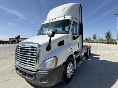 Truck cab with chrome grille and white Freightliner CA11364DC on a concrete lot; front-left view showing large mirrors, steps, and sleeper cab atop.