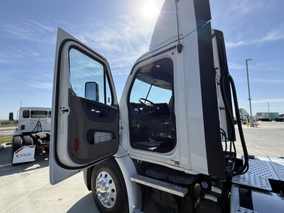 Truck cab door open showing Freightliner CA11364DC used conventional daycab, front wheel, and open interior with dashboard visible.